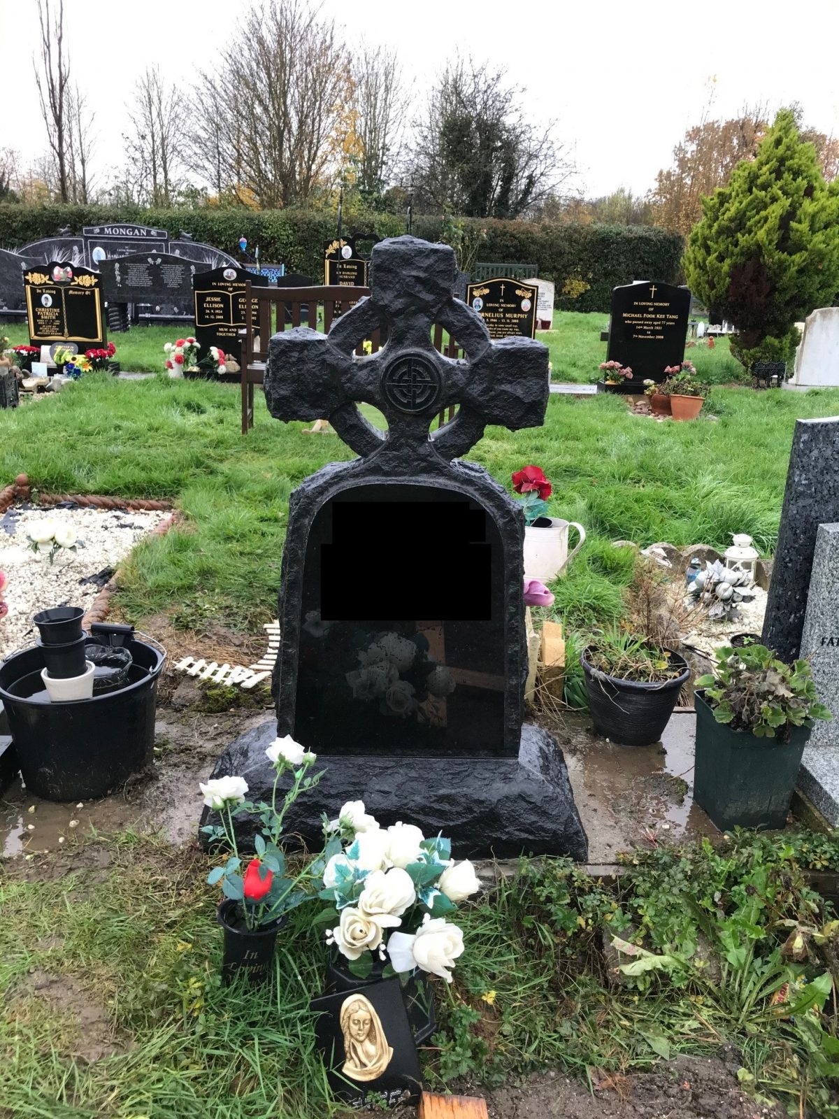 Sculptured black cross gravestone surrounded by white flowers