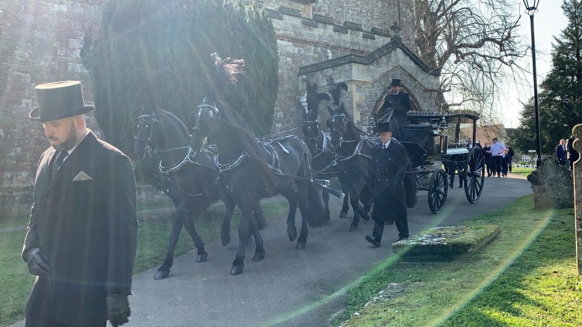 Black horse drawn carriage funeral leaving a church