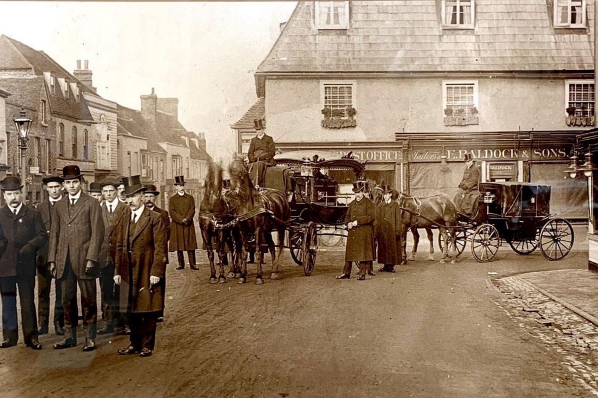 Old photograph taken in 1905 of two traditional horse drawn carriages surrounded by well dressed men